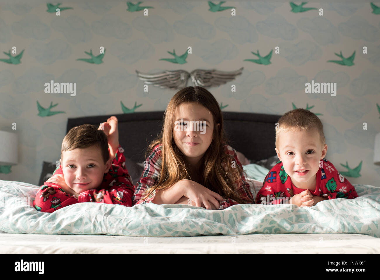 Brüder und Schwestern liegen auf Vorderseite auf Bett, Blick auf die Kamera zu Lächeln Stockfoto