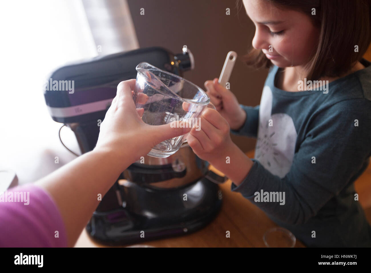 Junges Mädchen mit Rührgerät, Mutter Übergabe Tochter Messung Krug Stockfoto