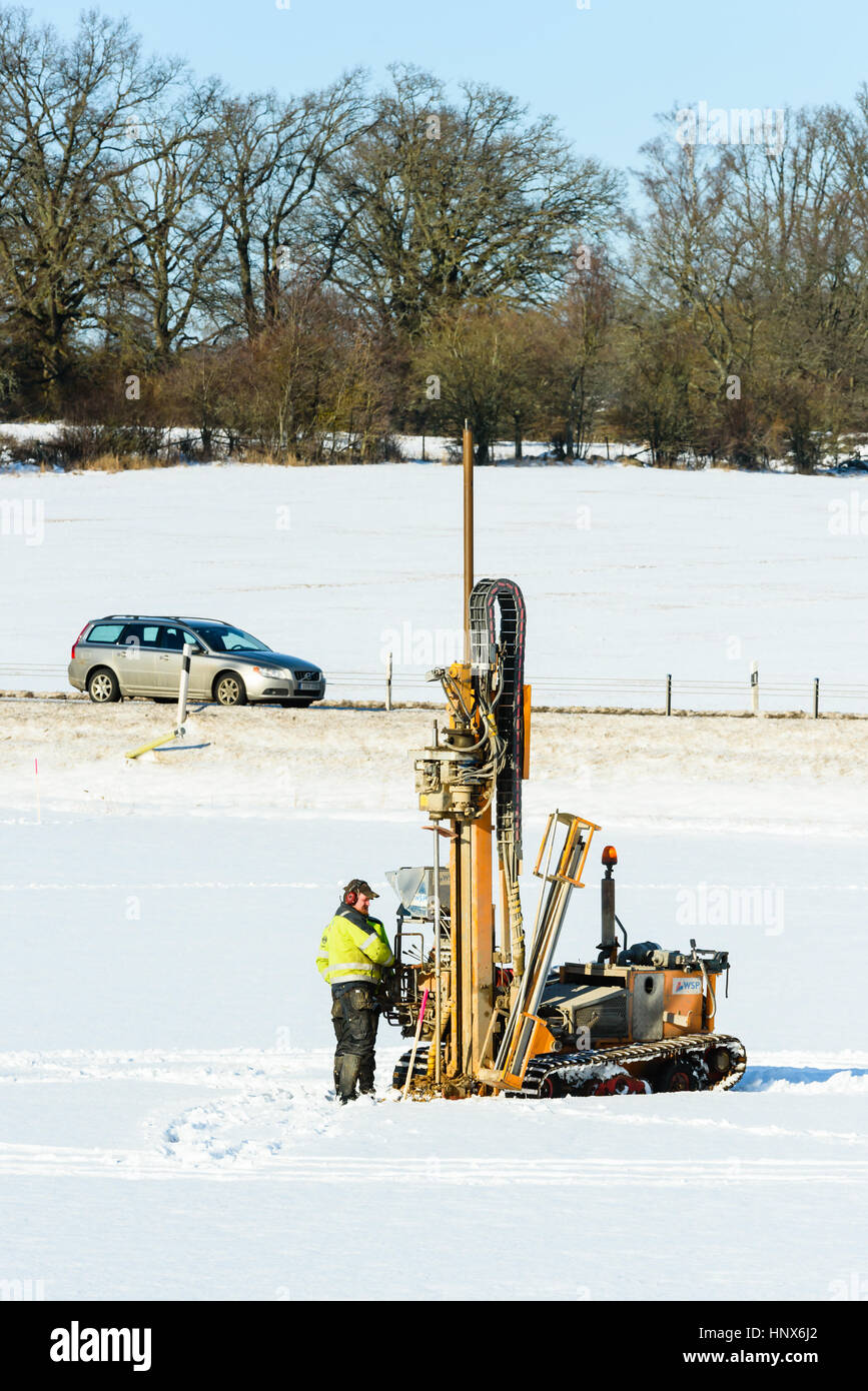 Lyckeby, Schweden - 13. Februar 2017: Real Life Dokumentarfilm von Explorationsbohrungen in der Erde auf einem schneebedeckten Feld mit Straße und Auto in staatlich Stockfoto