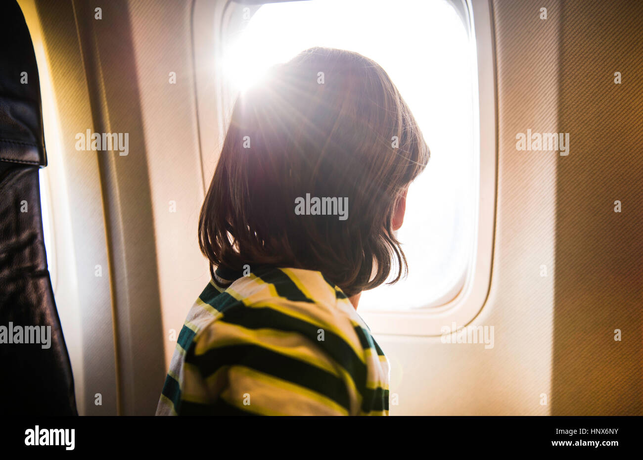 Boy am Flugzeug durch sonnendurchflutete Flugzeugfenster Stockfoto