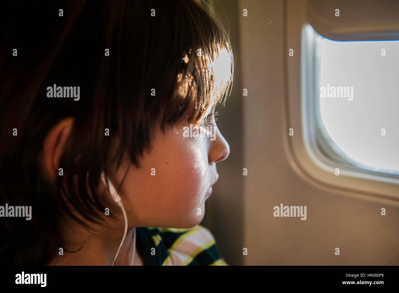 Boy am Flugzeug durch sonnendurchflutete Flugzeugfenster Stockfoto
