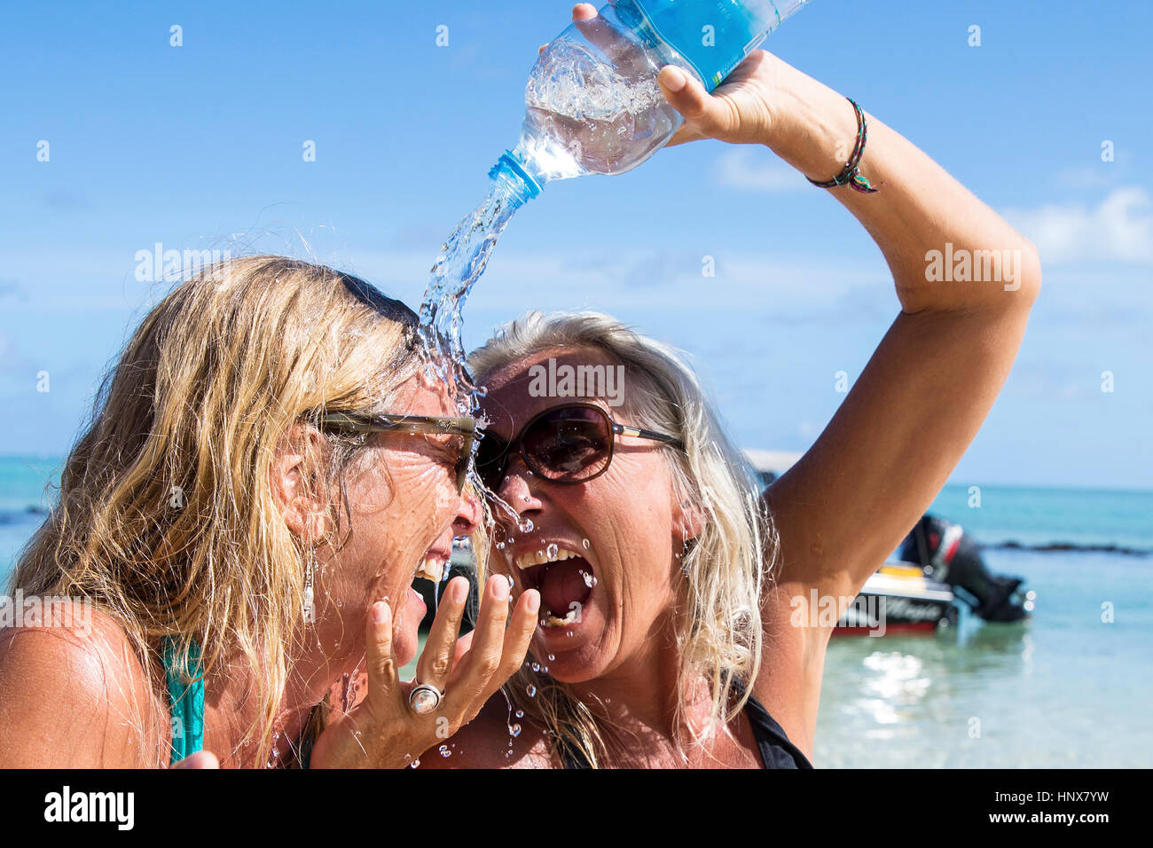 Reife weibliche Touristen gießen Wasser über Freund am Strand, Insel La Réunion Stockfoto