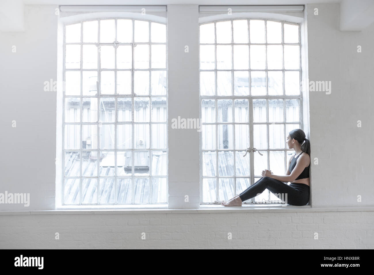 Frau sitzt auf der Fensterbank Blick aus Fenster Stockfoto