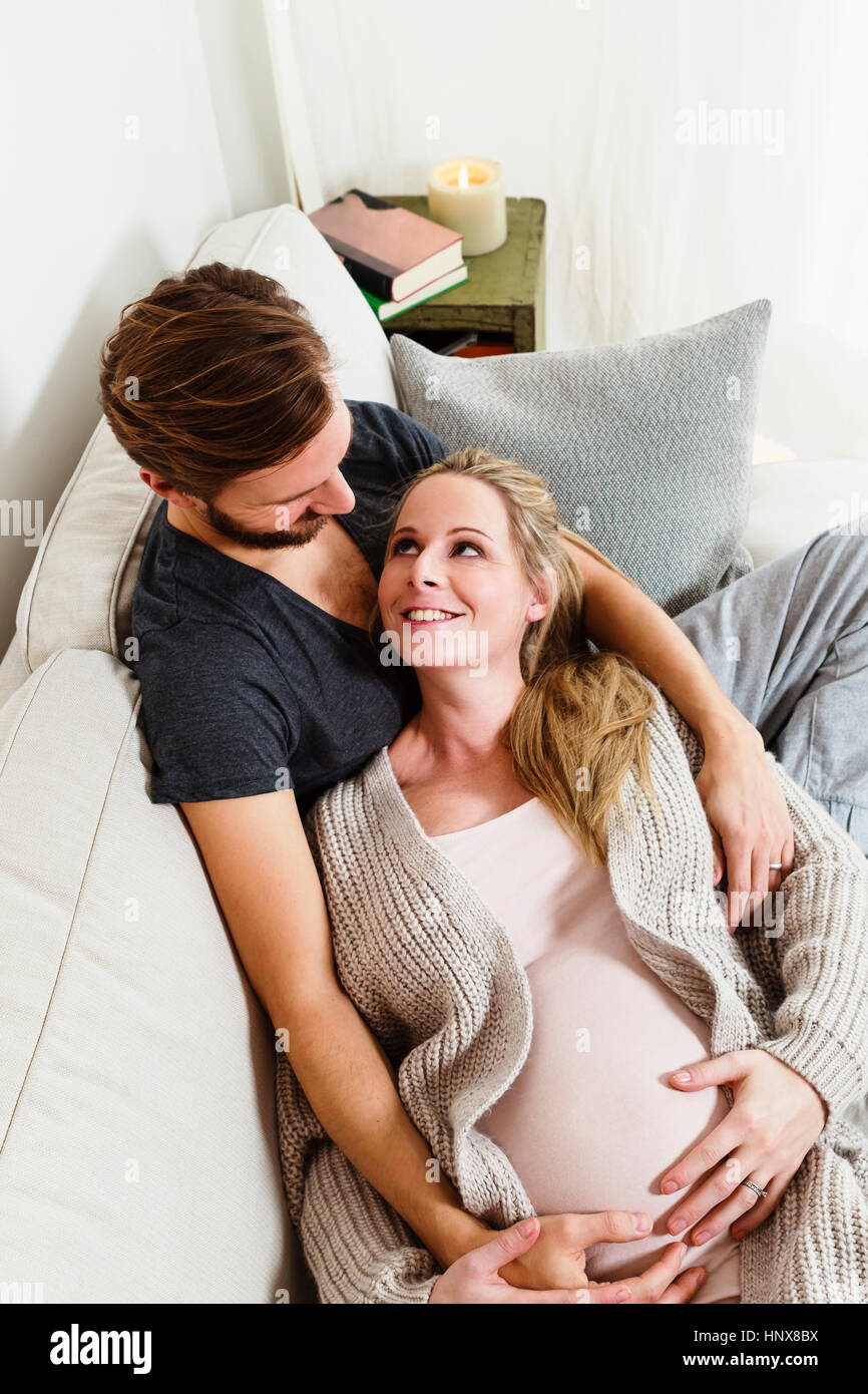 Schwanger Mitte erwachsenes paar berühren schwanger Bauch auf sofa Stockfoto