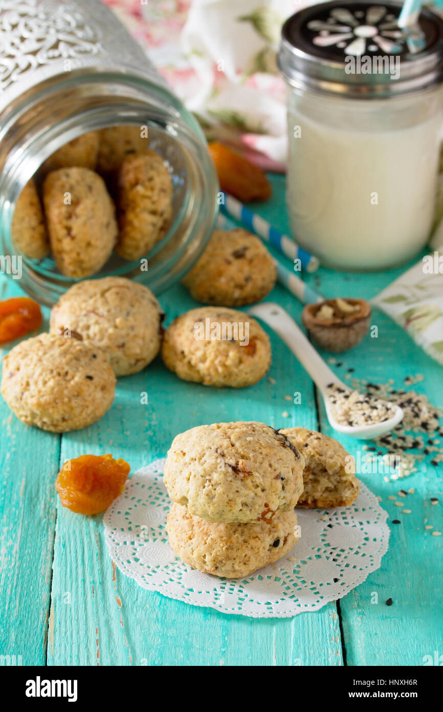 Gesunde Lebensmittel für das Frühstück. Hausgemachte Kekse aus Haferflocken mit Sesam, getrockneten Früchten, Nüssen in einem offenen Glas und Milch auf einem hölzernen Hinterg Stockfoto