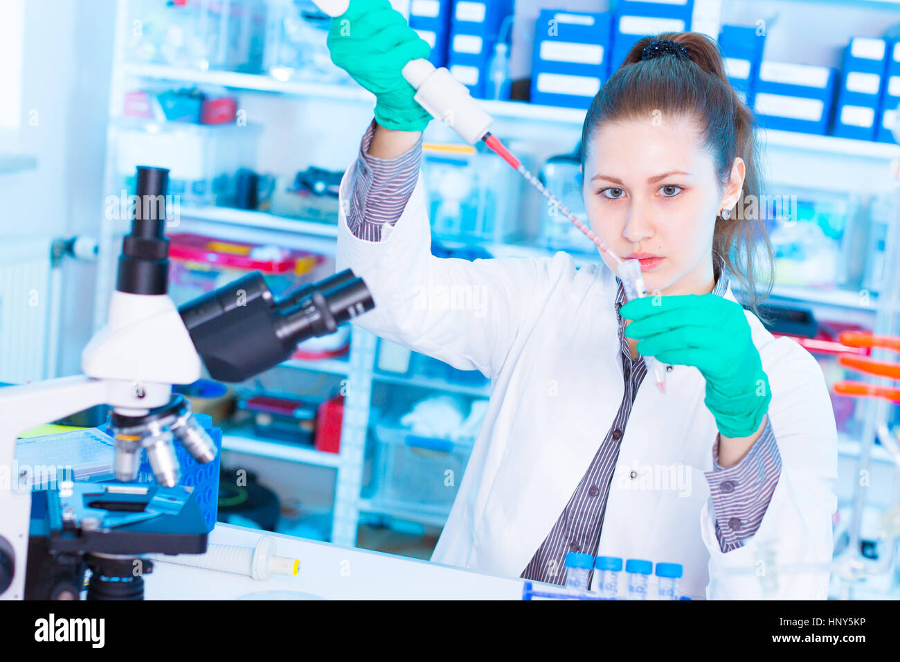 Ein junger Chemiker Reagenzglas mit Flüssigkeit während chemisches Experiment zu halten.  Assistent im Labor mit der Pipette Forschung von Krebsstammzellen.  Weiblich Stockfoto