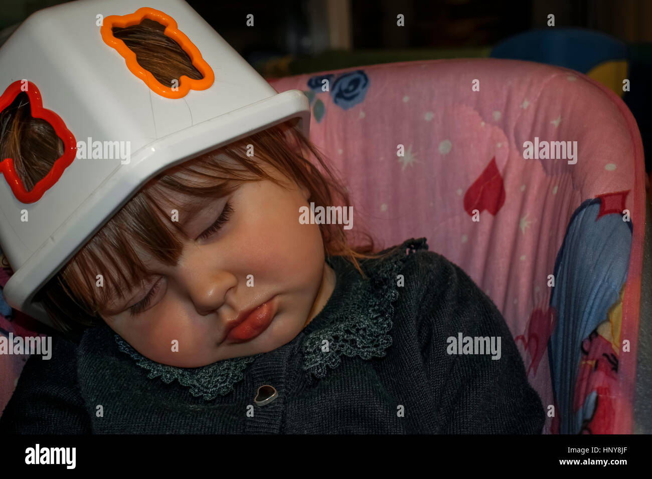 Blonde Mädchen schlafend auf einer Babyschaukel mit einem Kunststoff-Spielzeug-Box auf dem Kopf als Hut. Sie trägt eine schwarze Spitzenbluse Stockfoto