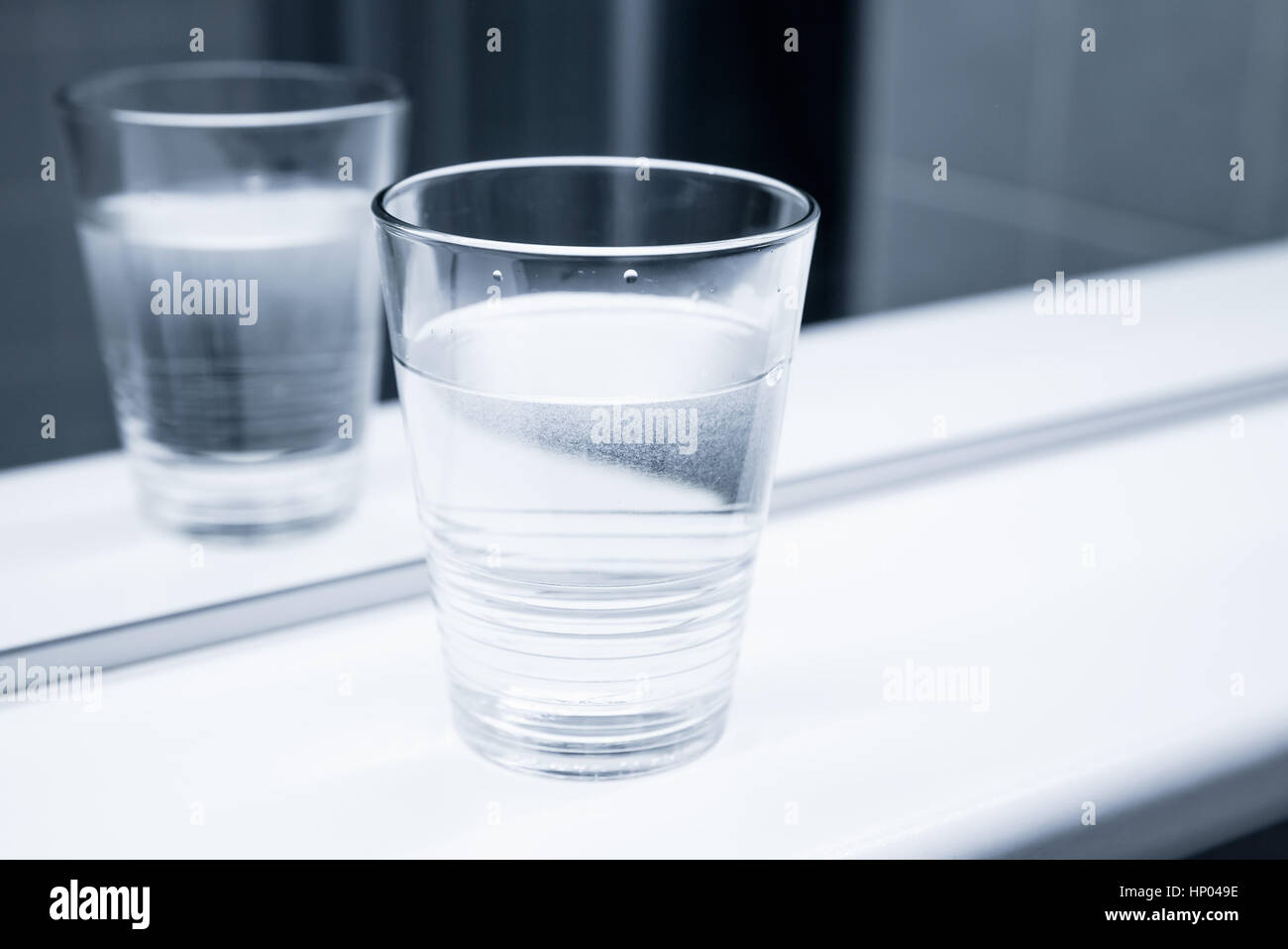 Glas Wasser stehen auf weißen Regal in der Nähe des Spiegels, blau getönten Nahaufnahme Foto Stockfoto