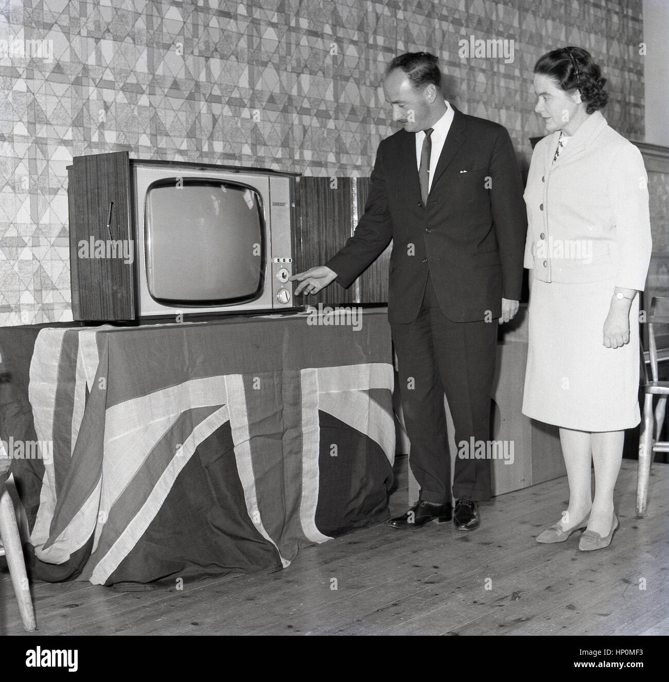 1964, historische, geschäftsführender Direktor der Rediffusion stolz zeigt sich der neue britische gemacht Fernseher aufgestellt auf einem Tisch, bedeckt mit einer "Union Jack"-Flagge, die sein Unternehmen in eine örtliche Schule gegeben haben. Stockfoto