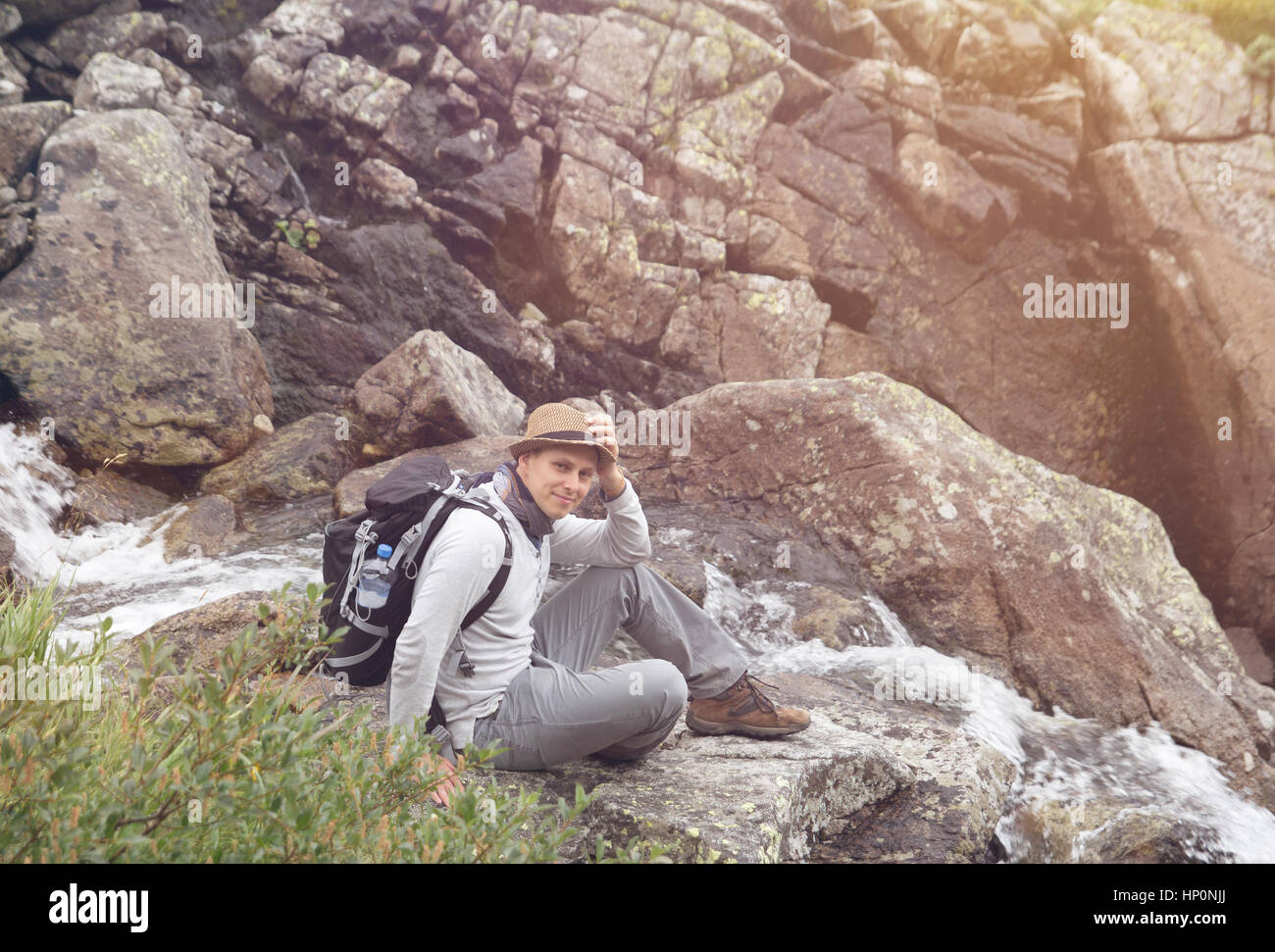 Wanderer-Mann mit Rucksack sitzt von Bergfluss Stockfoto