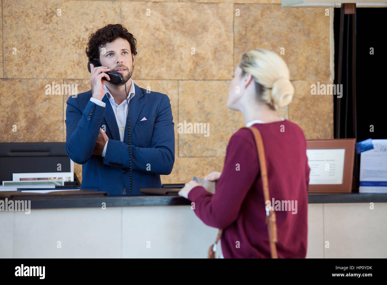 Ungeduldige Kunden warten während Hotel Angestellte an der Rezeption spricht am Telefon Stockfoto