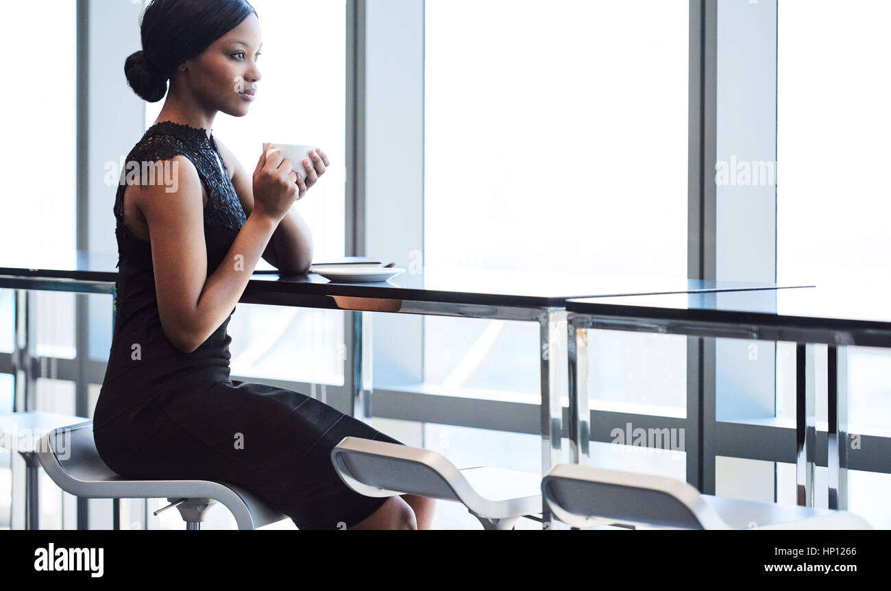 schwarze Frau sitzen auf großen Fensterplatz Barstuhl Stockfoto