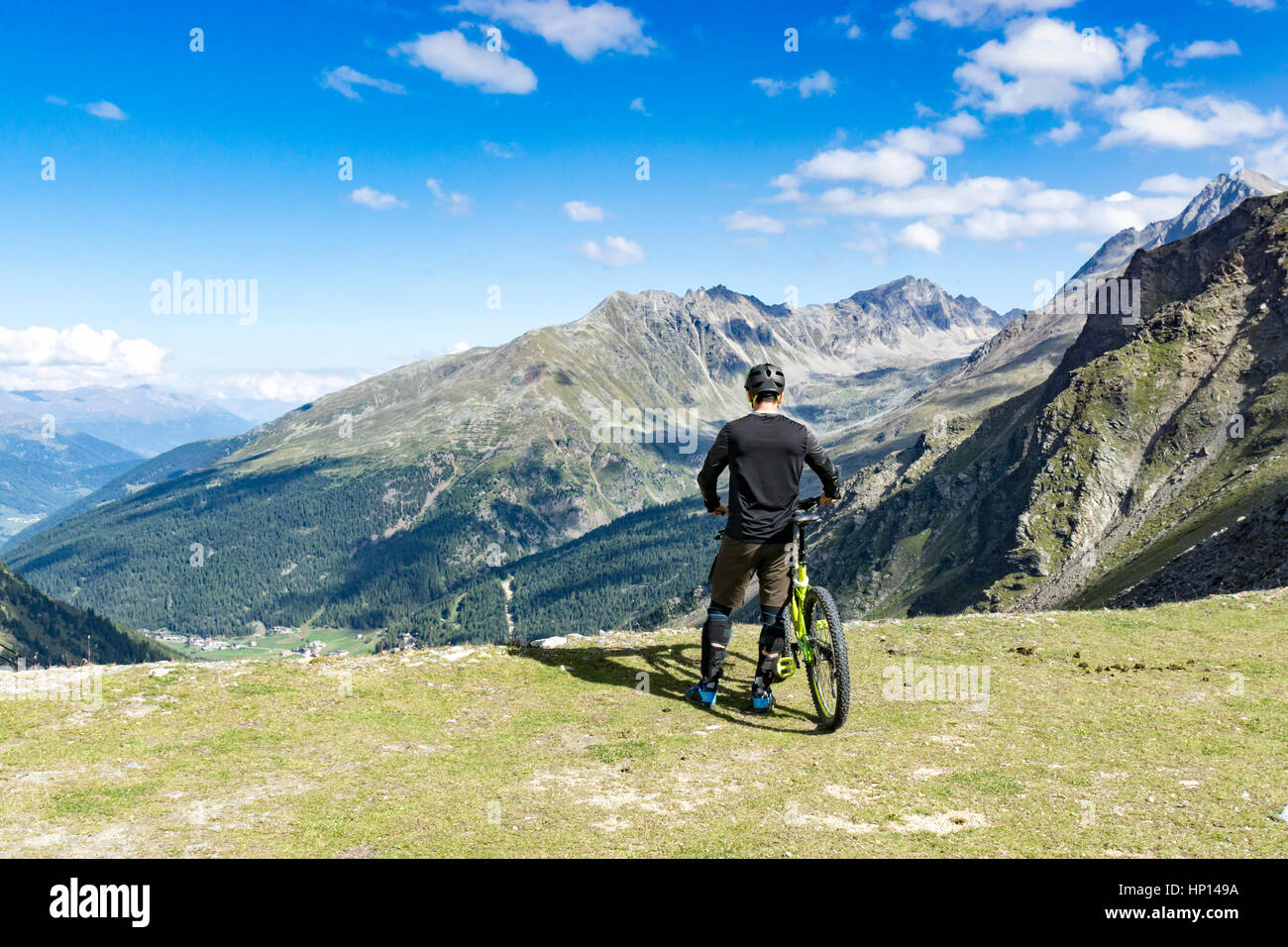 Mountainbiker steht am Rand eines Gipfels und genießt die Aussicht auf die Alpen Stockfoto