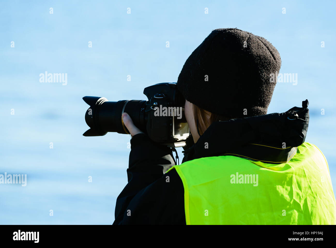 Junge weibliche Fotografin unter Bild von Ihnen entfernt. Sie trägt eine schwarze Kappe und eine leuchtend gelbe Weste. Hintergrund unscharf und sauber. Stockfoto