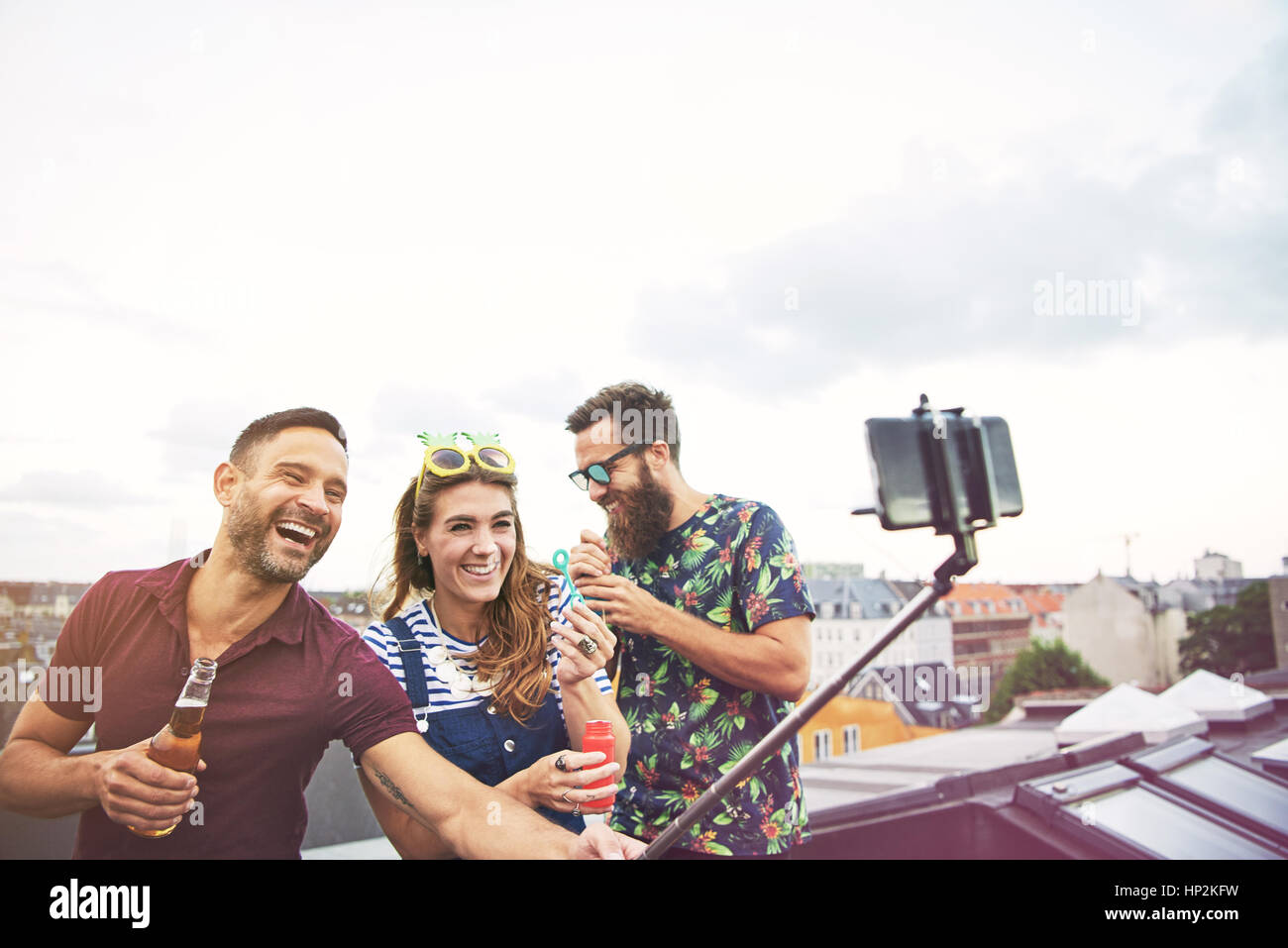 Drei glückliche Freunde fotografieren sich auf Dach beim trinken Bier und Seifenblasen Stockfoto