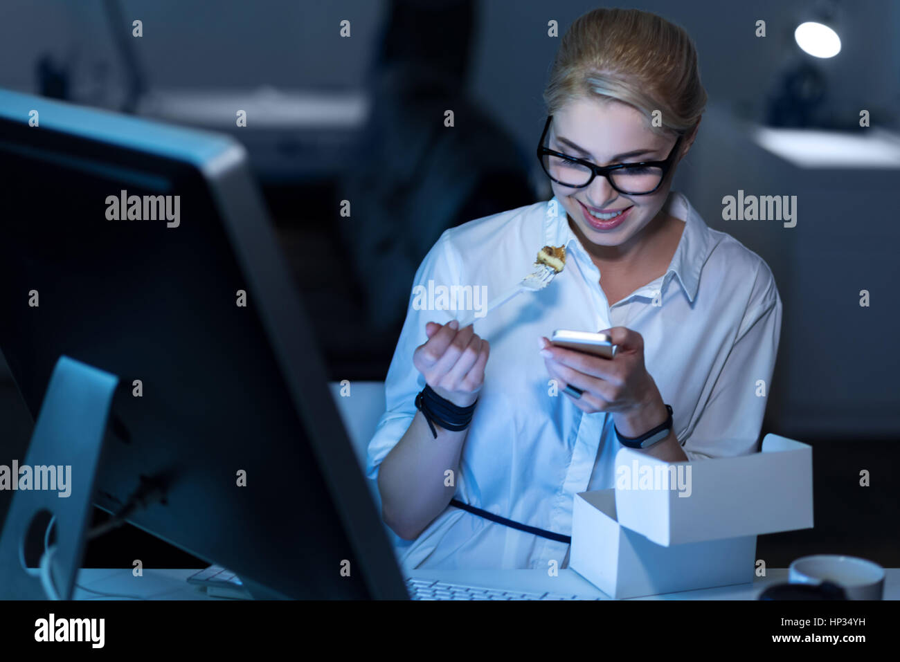 Fröhliche Sekretärin genießen Fast-Food am Arbeitsplatz Stockfoto