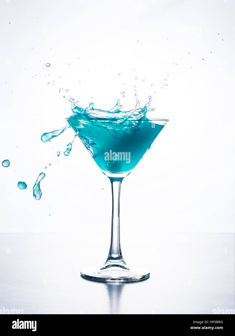 Blue Cocktail im Martiniglas mit Ice Cube Spritzwasser in Flüssigkeit vor weißem Hintergrund. Blue Curaçao cocktail mit Schuss auf weiß. Stockfoto