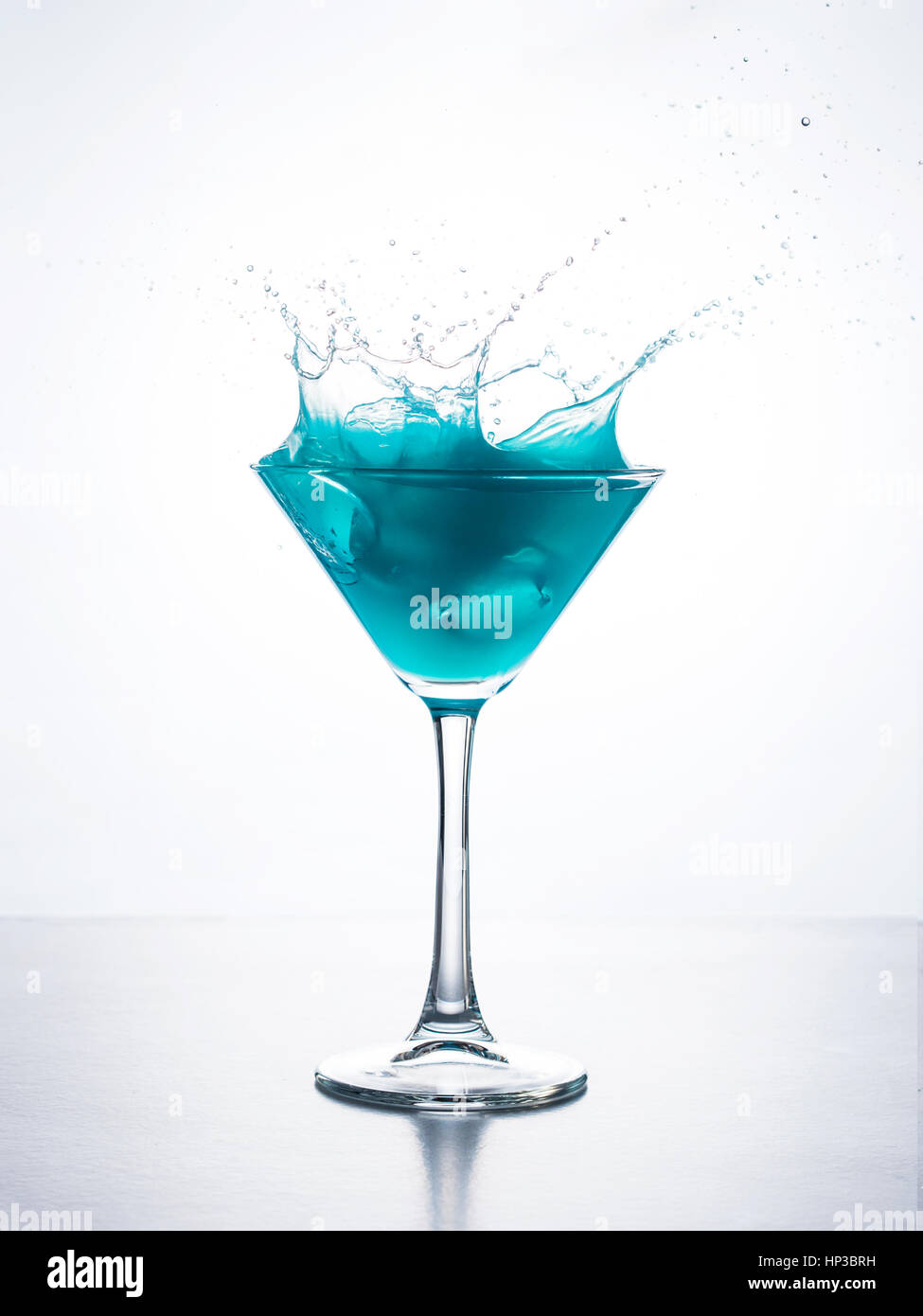 Blue Cocktail im Martiniglas mit Ice Cube Spritzwasser in Flüssigkeit vor weißem Hintergrund. Blue Curaçao cocktail mit Schuss auf weiß. Stockfoto