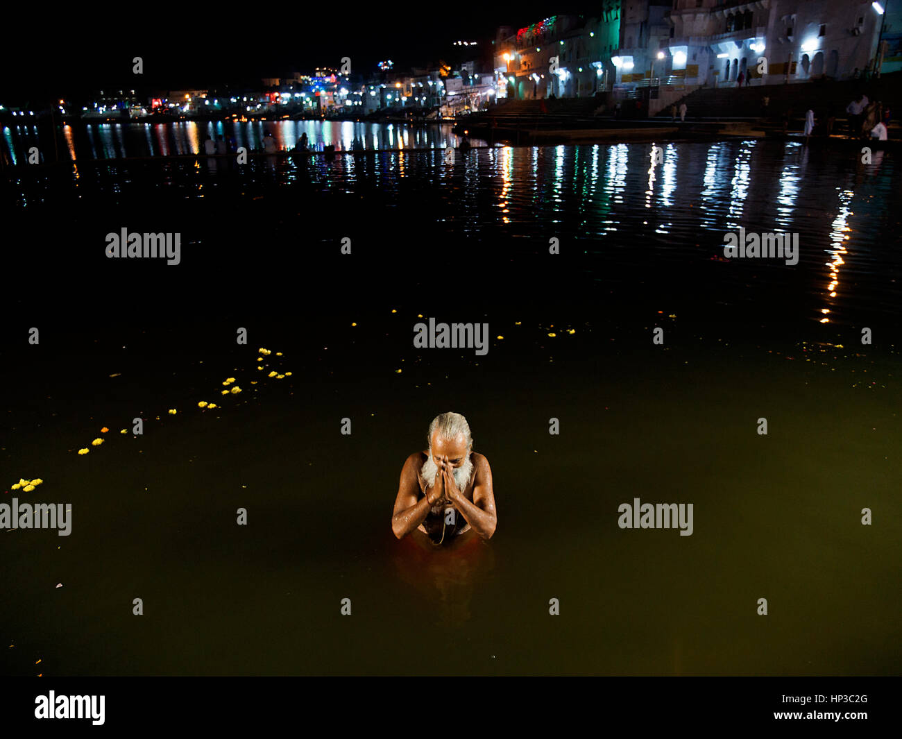 Ein Sadhu, die Hälfte ins Wasser eintaucht, Falten seine Hände in Pushkar-See in der Nacht, Wasser und Licht an den Ghats sichtbar Stockfoto
