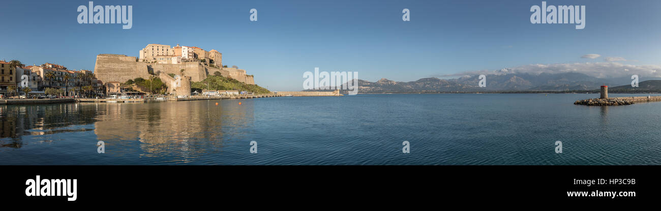 Panoramablick von der Zitadelle und Hafen Eingang in Calvi in Balagne Region Korsikas mit klaren, blauen Himmel und ruhigem Wasser und Schnee bedeckten Berg Stockfoto