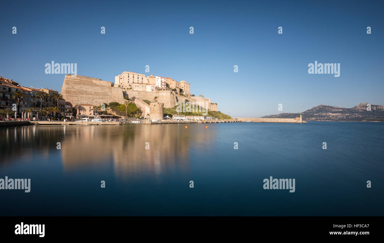 Slow-Shutter-Bild von der Zitadelle und Hafen Eingang in Calvi in der Balagne Region Korsikas mit klaren, blauen Himmel und glatte ruhigem Wasser Stockfoto