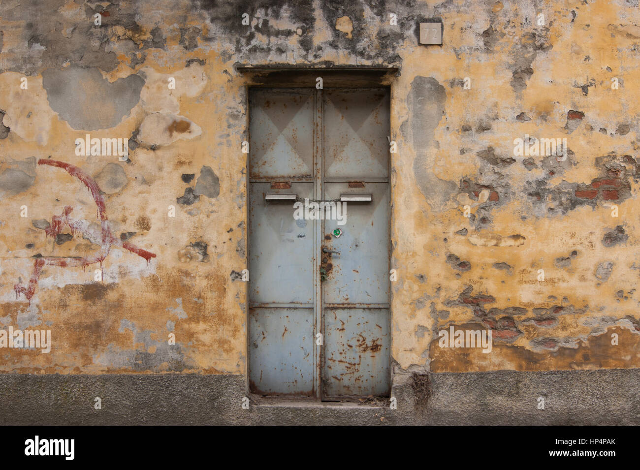 Alte rostige Metalltür mit Hammer und Sichel kommunistische Graffiti auf eine abgebrochene Mauer in Norditalien Stockfoto