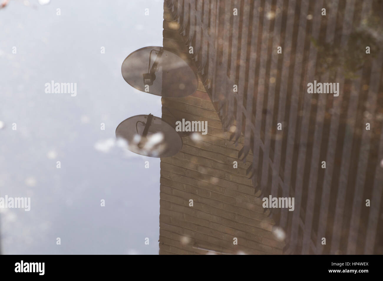 Reflexion in Pfütze von Mauer, Zaun und Satelliten-Gerichte. Stockfoto