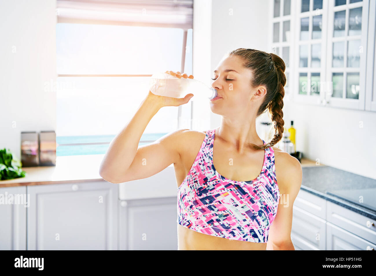 Junge sportliche Frau stehend auf Küche und Trinkwasser mit geschlossenen Augen. Stockfoto