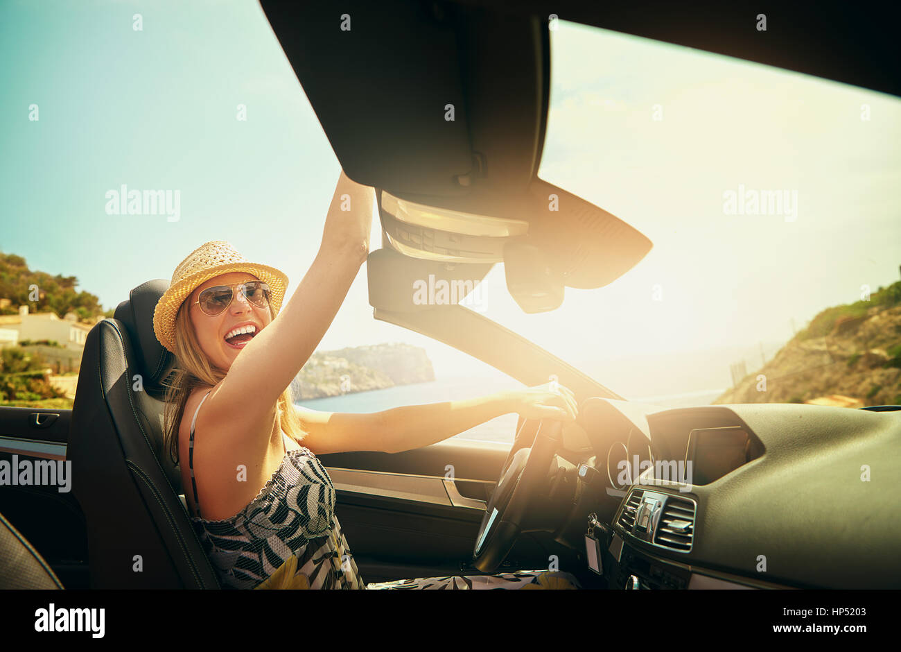 Lachend und begeistert Frau erreichen Hand über Dach während der Fahrt ihr Luxus versenkbare Top Auto im Sommer Stockfoto
