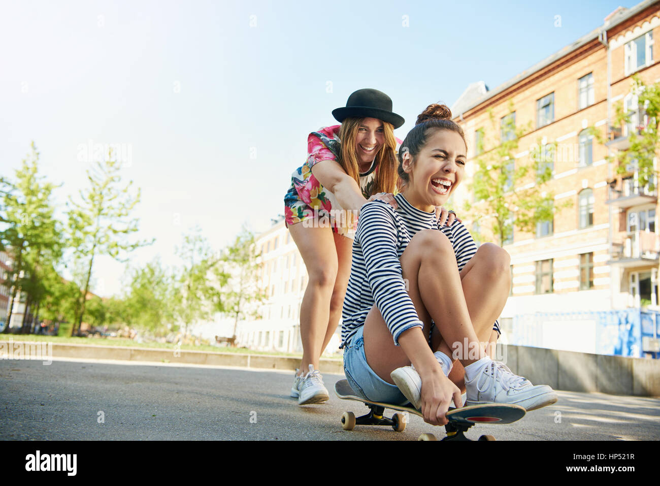 Niedrigen Winkel Blick auf glückliche teenaged Frau lachend Freund auf Skateboard unterwegs im Stadtgebiet mit Apartments, die um sie herum schieben Stockfoto