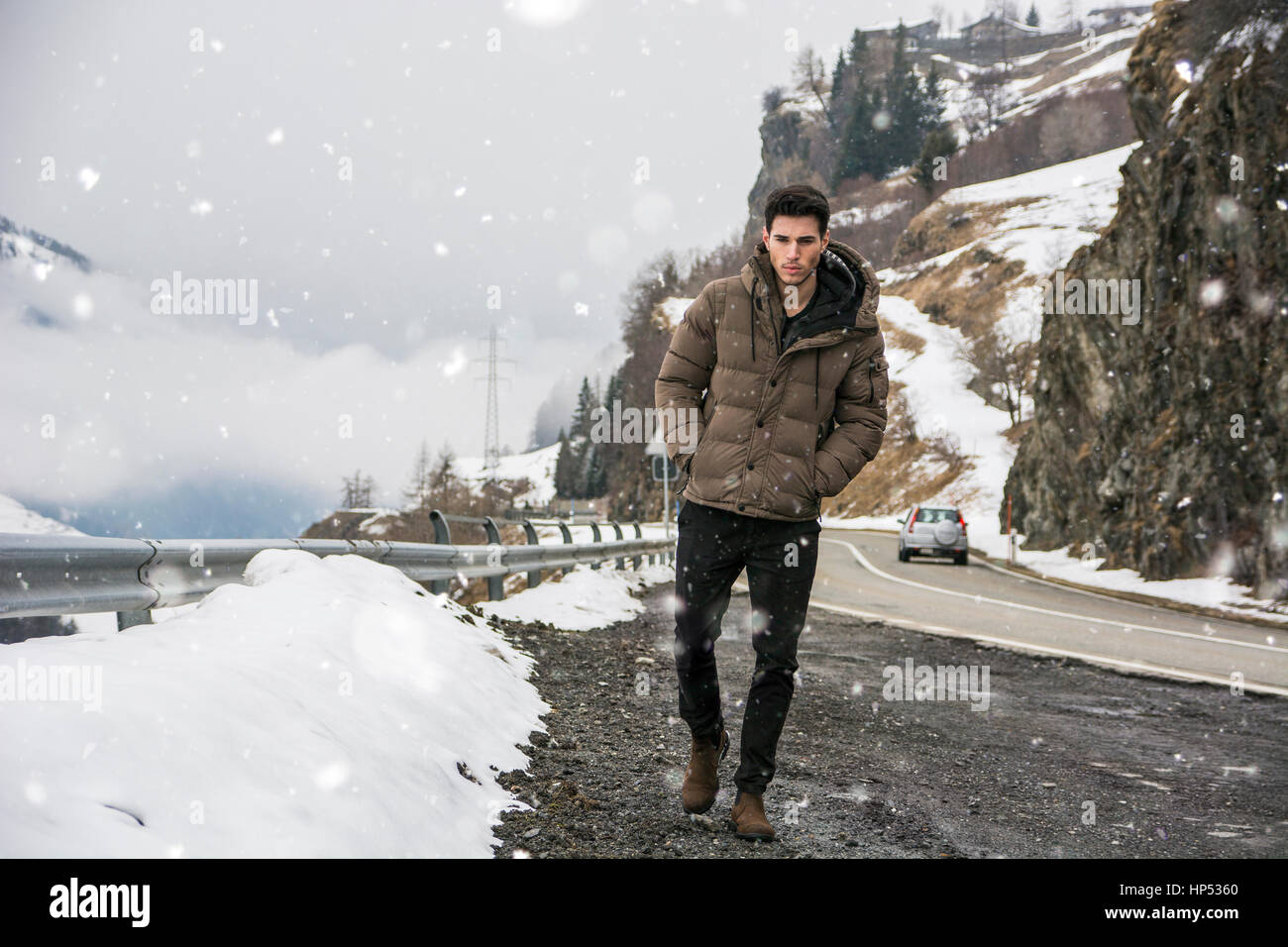 Junger Mann zu Fuß am Straßenrand unter dem Schnee in den Bergen. Verschneiten Bergen im Hintergrund Stockfoto