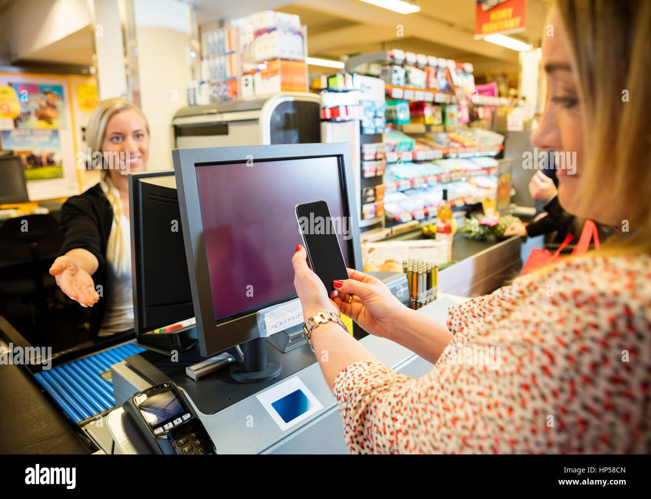 Kassierer gestikuliert während weibliche Kunde macht NFC Zahlung Stockfoto
