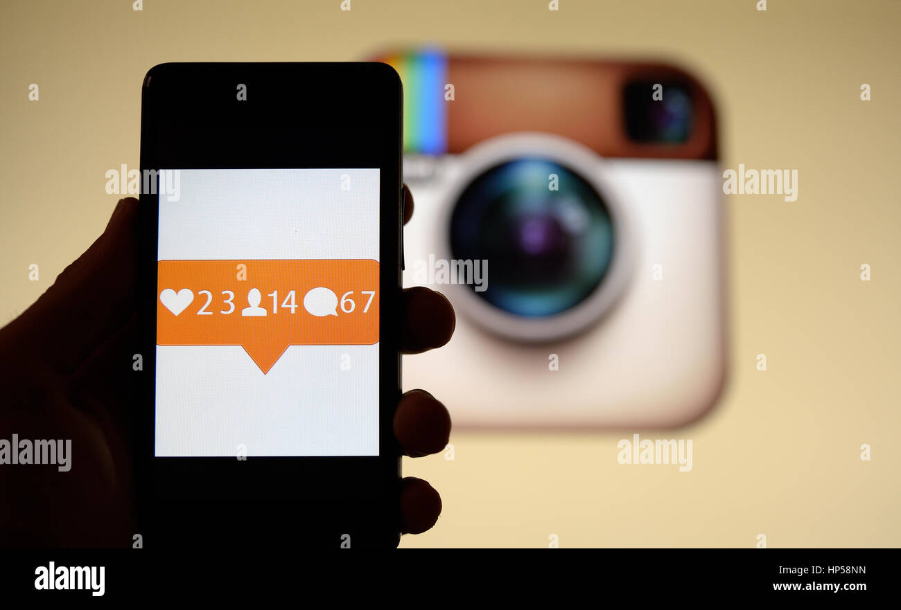 Hand, die ein Mobiltelefon mit Benachrichtigungen Bild drauf. Instagram Logo ist auf dem Hintergrund in einem Monitor angezeigt. Stockfoto