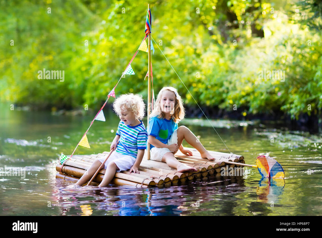 Zwei Kinder auf hölzerne Floß Fang von Fischen mit einem bunten Netz in einem Fluss und das Spiel mit Wasser am heißen Sommertag. Outdoor-Spaß und Abenteuer für Kinder. Stockfoto
