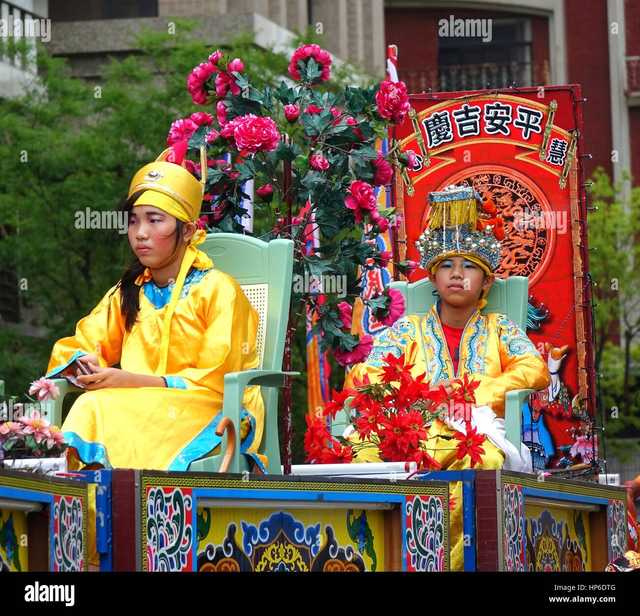 KAOHSIUNG, TAIWAN--9. Juli 2016: junge Menschen in traditionellen chinesischen Kostümen sitzen auf erhöhten Stühlen im taoistischen Prozession. Stockfoto