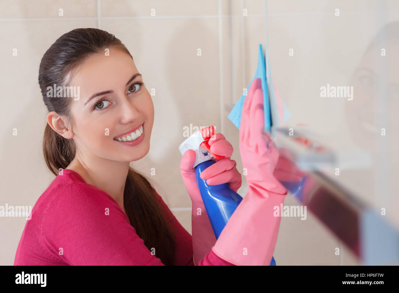 junge lächelnde Frau Reinigung Küche. Frau mit Flasche Spray Küche Polieren. Hände in Gummihandschuhe Stockfoto