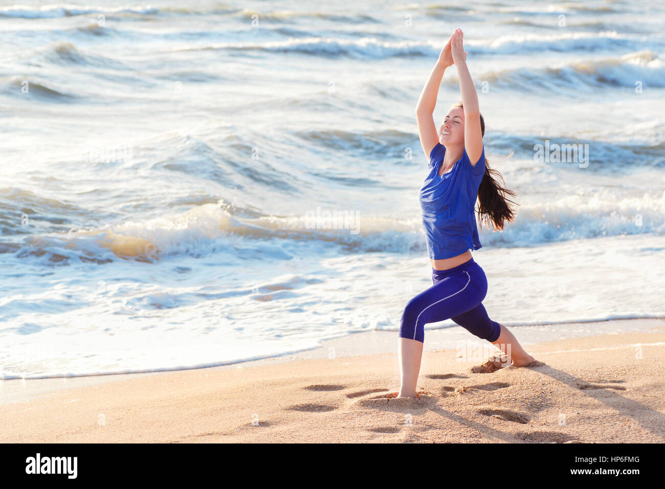 Frau praktizierender Krieger Yoga-Pose im Freien auf Sonnenaufgang am Meer oder Ozean Hintergrund. Frauen tun Yoga-Krieger oder Virabhadrasana Pose am Strand mit Stockfoto