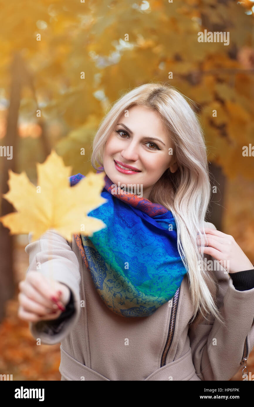 Mädchen halten Herbst orange Ahornblatt. Porträt von schöne junge blonde Frau mit Ahornblatt in der Hand, verbringen Zeit im Herbst Park mit Sonnenschein Stockfoto