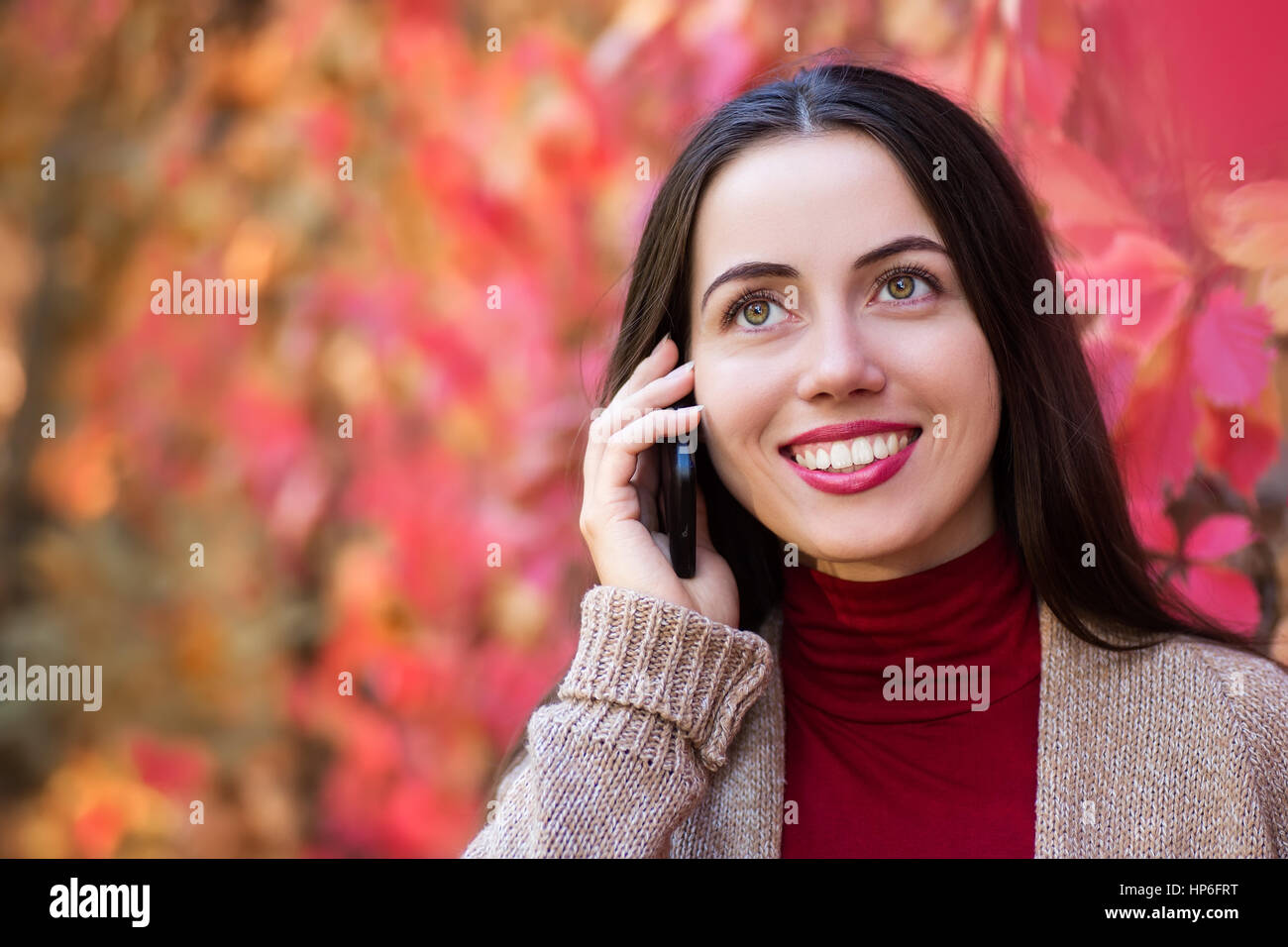 Lächelnde Mädchen reden über Handy im Herbst Park. Fröhliche Frau spricht auf einem Smartphone im Freien in eine leuchtend rote Blätter im Herbst. Portra Stockfoto