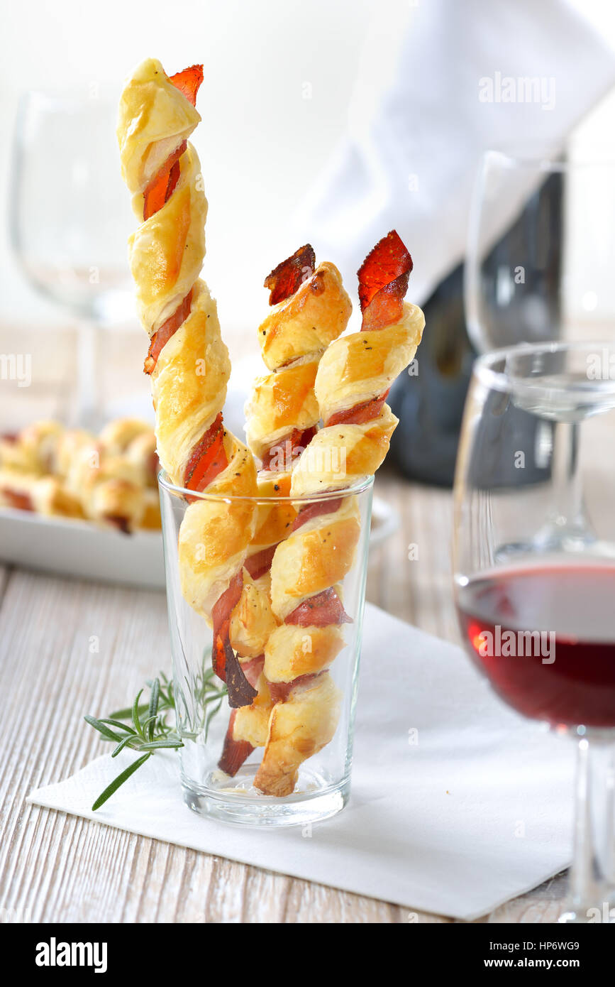 Gebackene herzhafte Blätterteig-sticks mit Schinken und Kräutern, serviert mit einem Glas Rotwein Stockfoto