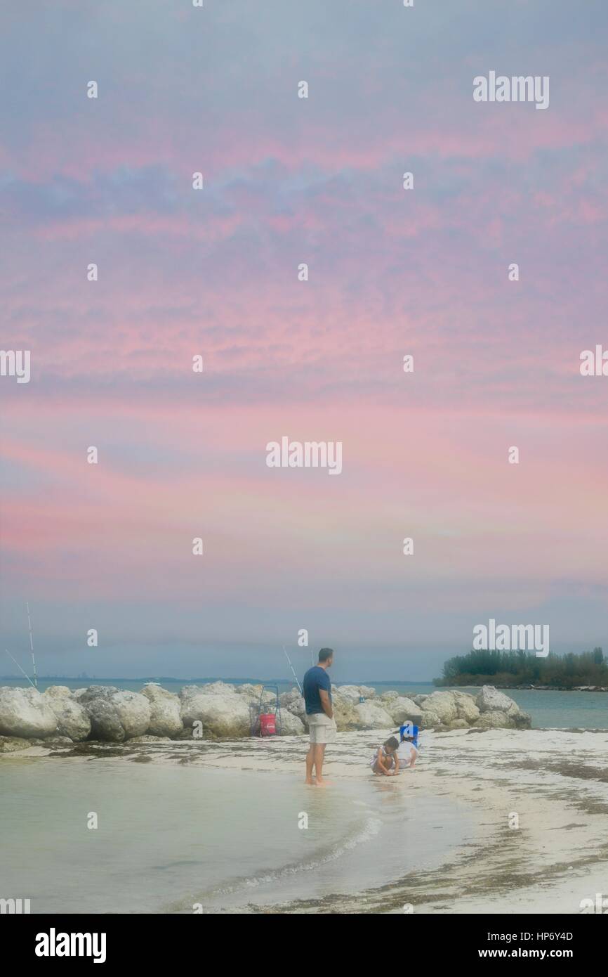 Vater und Sohn spielen am Strand mit einem bunten Himmel Stockfoto