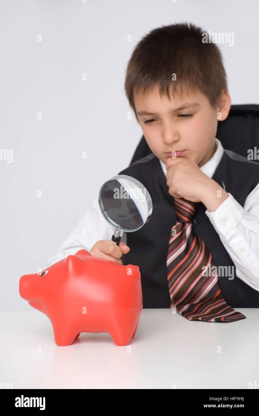 Model Release, Kleiner Geschaeftsmann, 8, Betrachtet Sparschwein Durch sterben Lupe - kleine Businesman beobachten Piggy Bank unter der Lupe Stockfoto