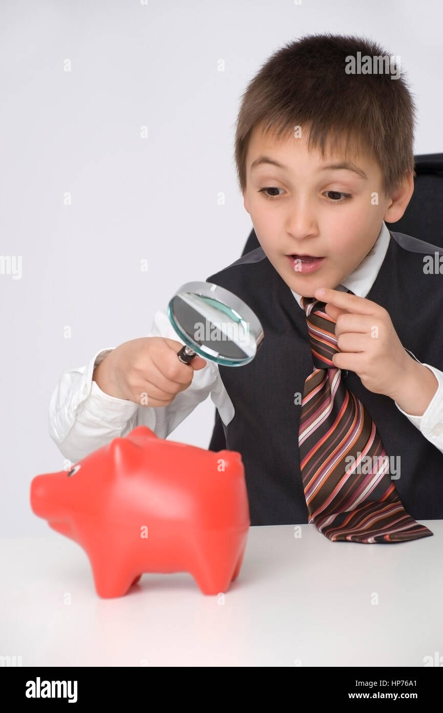 Model Release, Kleiner Geschaeftsmann, 8, Betrachtet Sparschwein Durch sterben Lupe - kleine Businesman beobachten Piggy Bank unter der Lupe Stockfoto