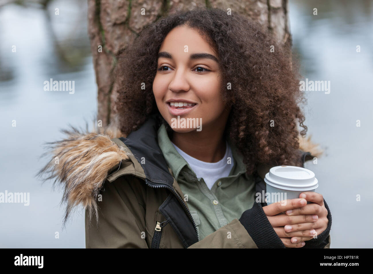 Schöne glückliche Mischlinge afroamerikanische Mädchen Teenager weibliche junge Frau lächelt, trinken Kaffee zum Mitnehmen außerhalb Stockfoto