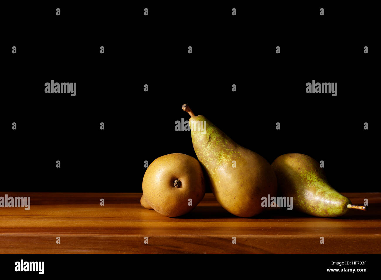 Studie über drei grüne Konferenz Birnen auf einer Holzfläche mit Seitenlicht im malerischen Stil mit schwarzem Hintergrund angeordnet. Stockfoto