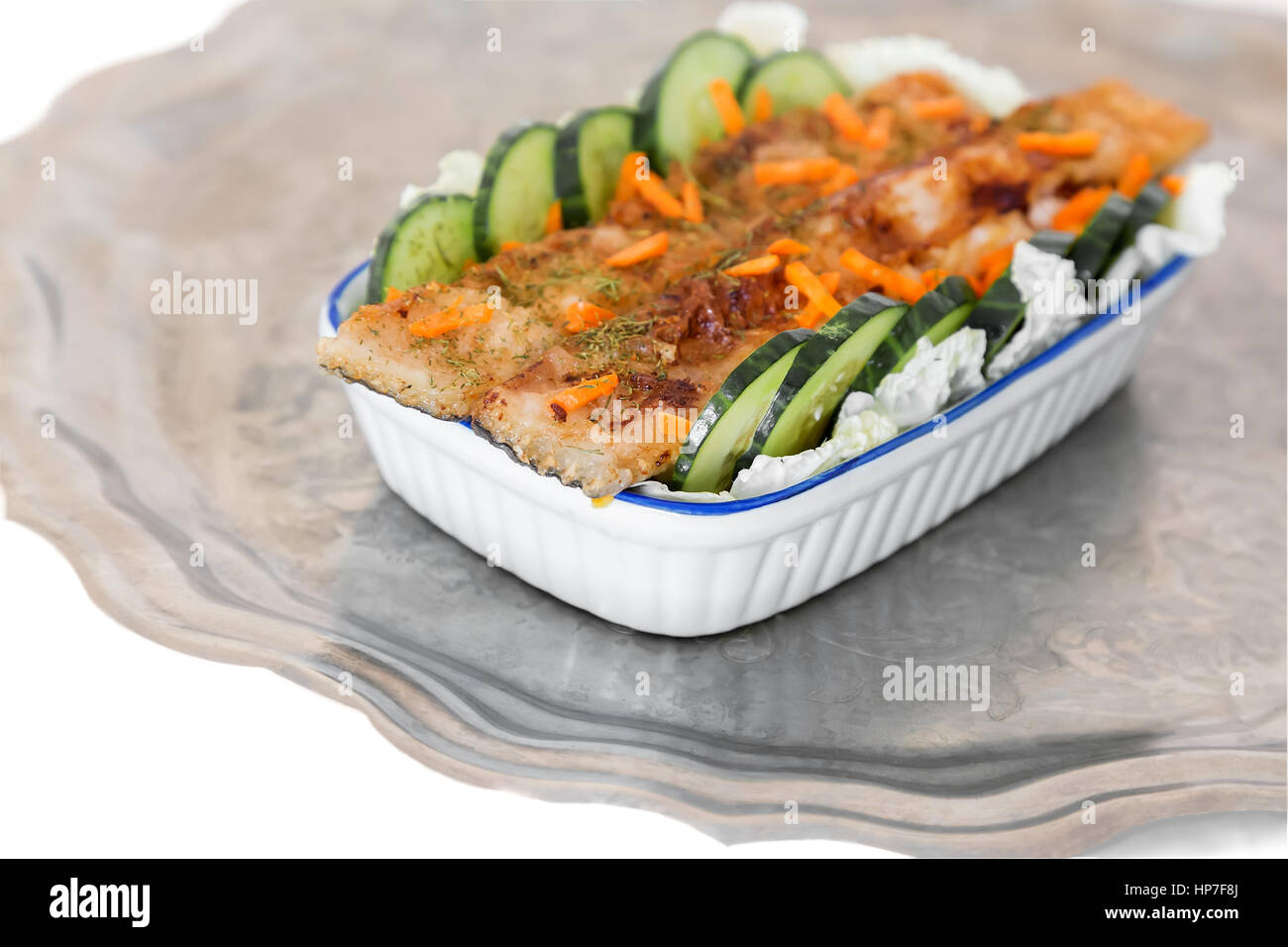 In einer Keramikschale auf dem Tisch gebratener Fisch mit Salat und Gurke. Gerichte mit Fisch ist auf einem Metalltablett. Stockfoto