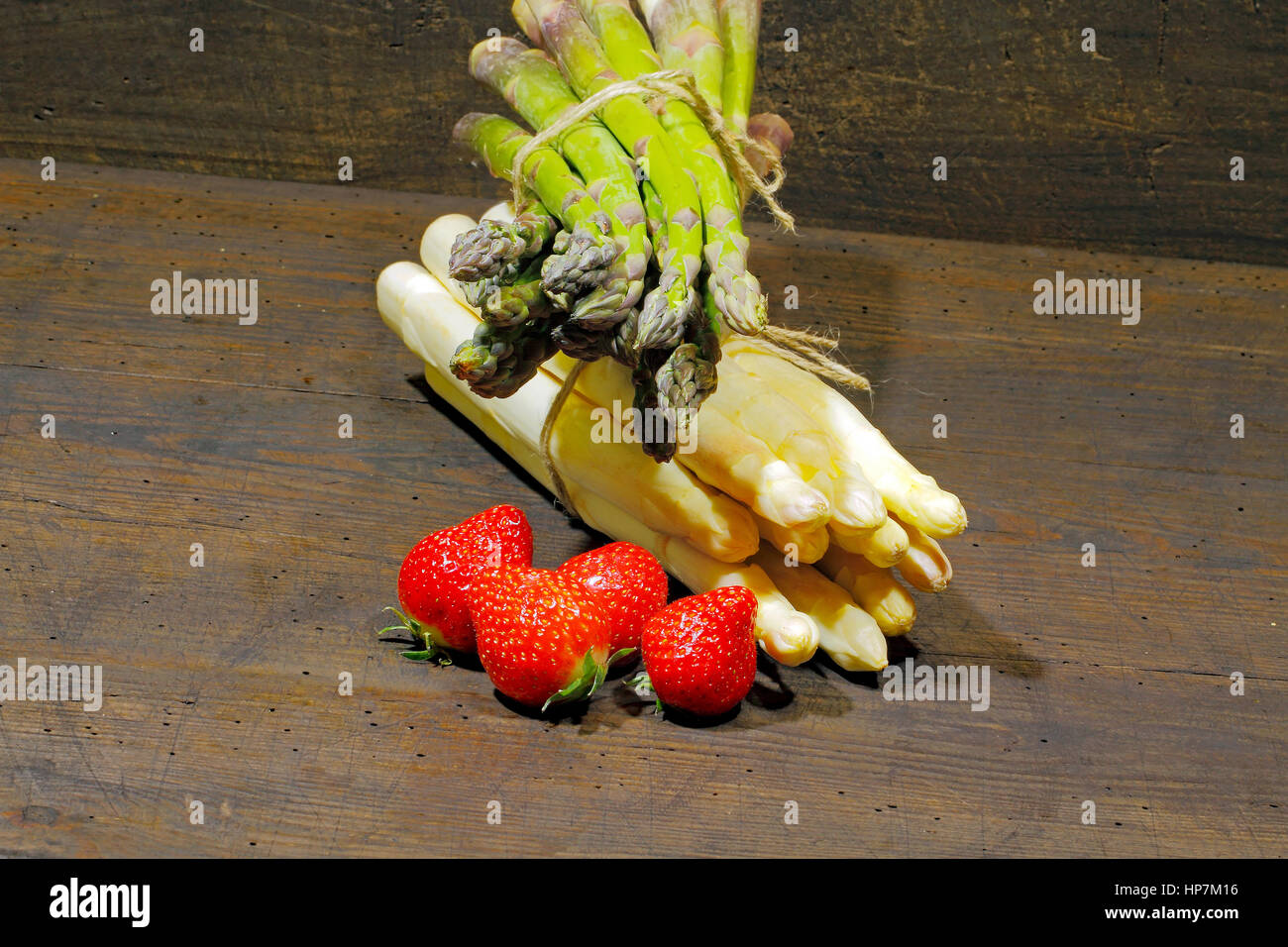 Erntefrische Spargel und Erdbeeren auf einem urigen, alten Holzbrett Stockfoto