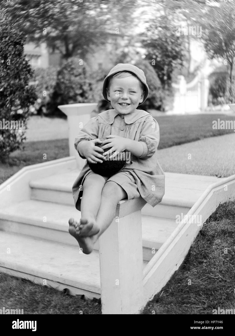 Victorian Foto von einem lächelnden jungen Kind in einem formalen Garten saß auf einem kurzen konkreten post Holding eine Kugel an der Unterseite der Garten Schritte. Um 1910 Stockfoto