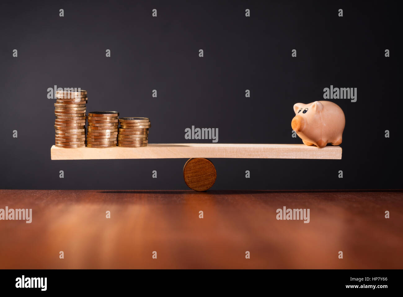 Wippe mit Piggy Bank auf der einen Seite und Stapel von Geld auf der anderen Seite. Stockfoto