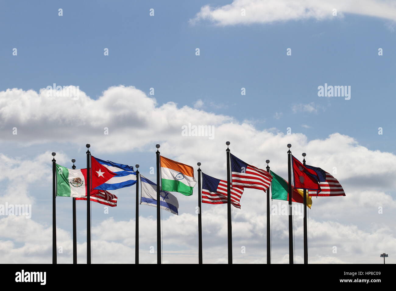 Die Flaggen USA, Nepal, Kamerun, Israel, Indien, Mexiko und Kuba auf einen Fahnenmasten im Wind gegen einen blauen Himmel und weiße Wolken. Der Wind weht. Stockfoto